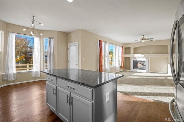 kitchen featuring gray cabinetry, dark stone counters, ceiling fan, stainless steel fridge, and a kitchen island