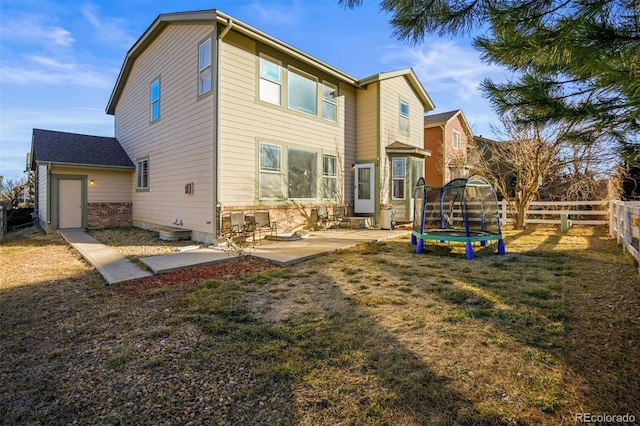 back of property with a trampoline, a patio area, and a lawn