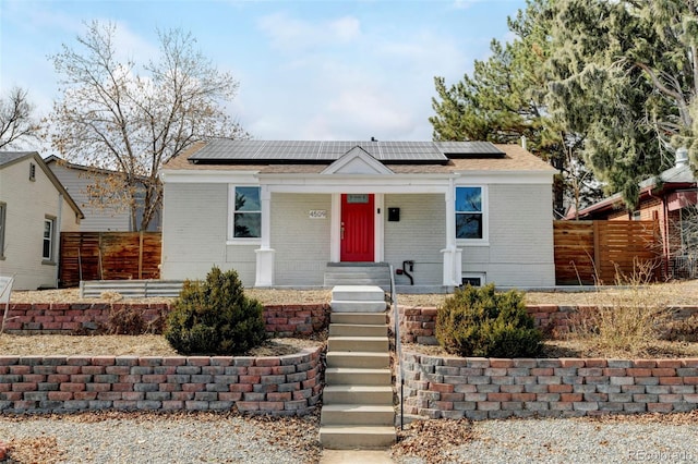 bungalow-style home featuring brick siding, fence, and roof mounted solar panels