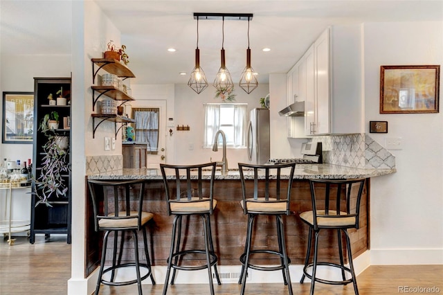 kitchen featuring a peninsula, light wood-style floors, white cabinetry, and freestanding refrigerator