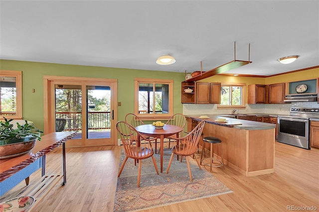 kitchen with stainless steel electric stove, plenty of natural light, kitchen peninsula, and light hardwood / wood-style flooring