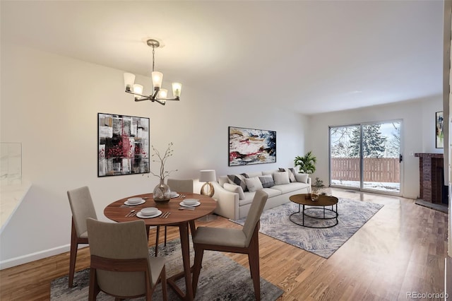 dining room featuring a notable chandelier, hardwood / wood-style flooring, and a brick fireplace