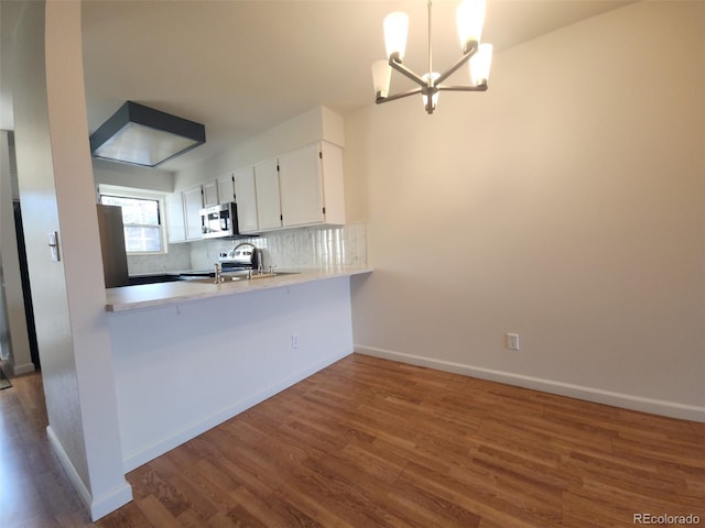 kitchen featuring white cabinetry, backsplash, hanging light fixtures, stainless steel appliances, and dark wood-type flooring