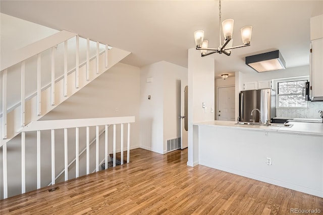 kitchen with sink, stainless steel fridge, white cabinetry, decorative light fixtures, and light wood-type flooring