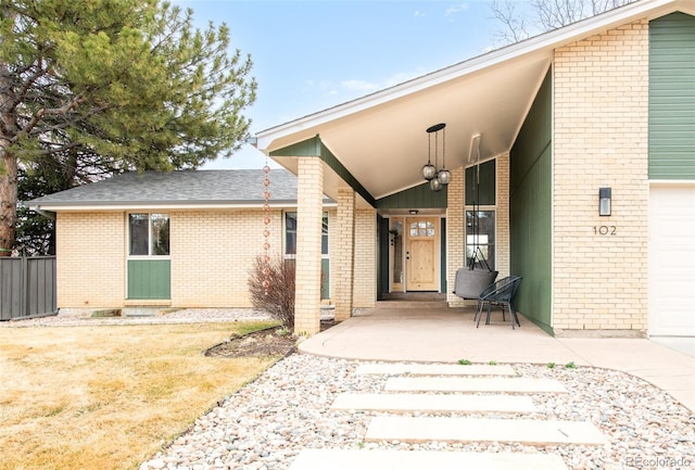 doorway to property with a garage, brick siding, and a shingled roof