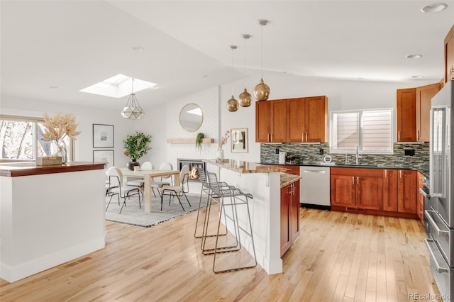 kitchen featuring a breakfast bar, vaulted ceiling with skylight, light wood-style floors, stainless steel appliances, and a sink