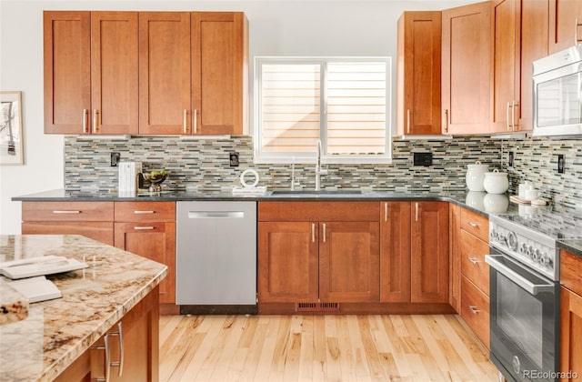 kitchen featuring a sink, dark stone counters, light wood finished floors, and stainless steel appliances