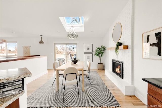 dining room featuring lofted ceiling with skylight, a healthy amount of sunlight, a fireplace, and light wood-style floors