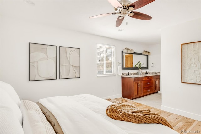 bedroom with ensuite bath, light wood-style flooring, a ceiling fan, and baseboards