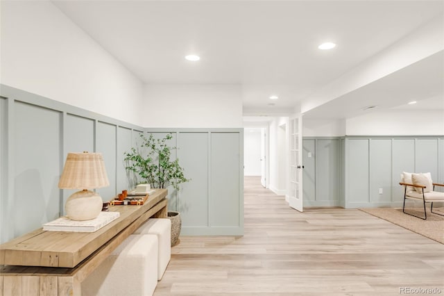 corridor with a decorative wall, recessed lighting, light wood-style flooring, and a wainscoted wall