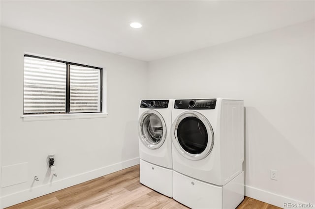 clothes washing area featuring washing machine and clothes dryer, laundry area, light wood finished floors, and baseboards