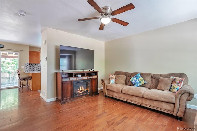 12333 Newport Ct, Brighton, CO 80602 - living area featuring light wood-type flooring, a ceiling fan, baseboards, and a glass covered fireplace