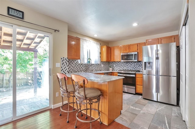 12333 Newport Ct, Brighton, CO 80602 - kitchen featuring appliances with stainless steel finishes, a peninsula, light countertops, tasteful backsplash, and a kitchen bar