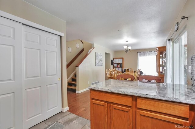 12333 Newport Ct, Brighton, CO 80602 - kitchen with decorative light fixtures, light stone countertops, a peninsula, a chandelier, and brown cabinets