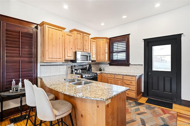 kitchen with sink, stove, a kitchen breakfast bar, light stone counters, and wood-type flooring