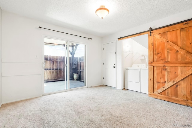 carpeted empty room with washer and clothes dryer, a barn door, baseboards, and a textured ceiling