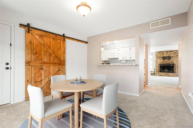 dining area with a fireplace, visible vents, a barn door, baseboards, and light carpet