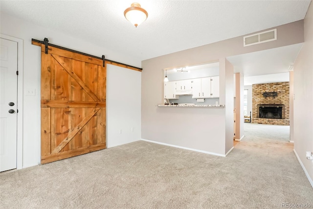 unfurnished living room with a barn door, a brick fireplace, visible vents, and light colored carpet