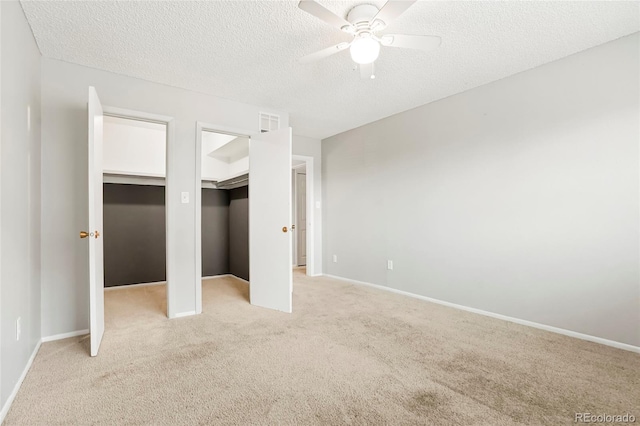 unfurnished bedroom featuring a ceiling fan, a textured ceiling, two closets, baseboards, and light carpet