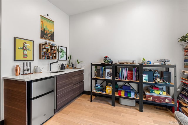 bar featuring refrigerator, dark brown cabinetry, light wood-type flooring, and sink