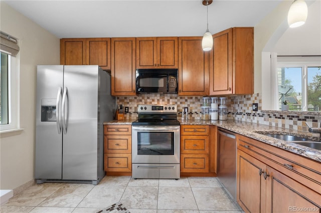 9960 Garland Ln, Broomfield, CO 80021 - kitchen with stainless steel appliances, brown cabinetry, tasteful backsplash, light stone counters, and decorative light fixtures