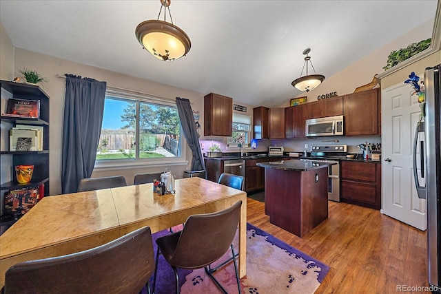 kitchen with hanging light fixtures, wood-type flooring, vaulted ceiling, a kitchen island, and appliances with stainless steel finishes