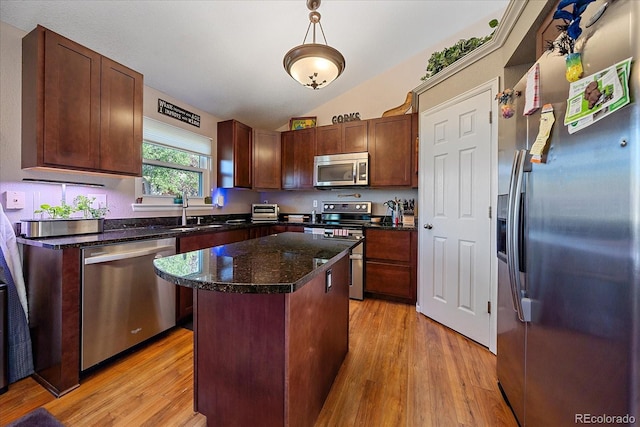 kitchen with appliances with stainless steel finishes, vaulted ceiling, decorative light fixtures, a center island, and light hardwood / wood-style floors