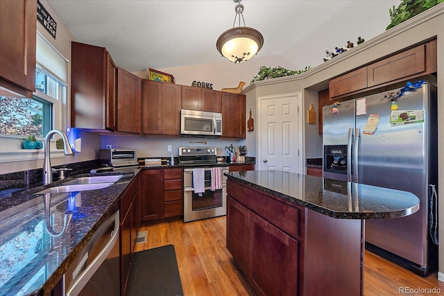 kitchen with sink, vaulted ceiling, dark stone countertops, light wood-type flooring, and stainless steel appliances