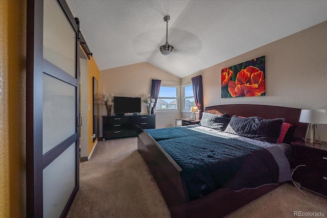 carpeted bedroom with a textured ceiling, a barn door, vaulted ceiling, and ceiling fan