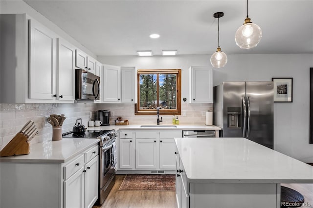 kitchen with a kitchen island, hanging light fixtures, stainless steel appliances, sink, and white cabinetry