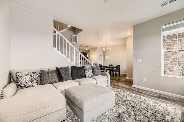 living area with a notable chandelier, visible vents, stairs, and wood finished floors