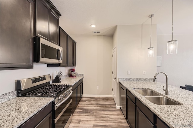 kitchen featuring baseboards, light stone countertops, light wood-type flooring, stainless steel appliances, and a sink