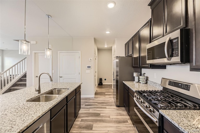 kitchen featuring decorative light fixtures, light wood-type flooring, light stone counters, appliances with stainless steel finishes, and a sink