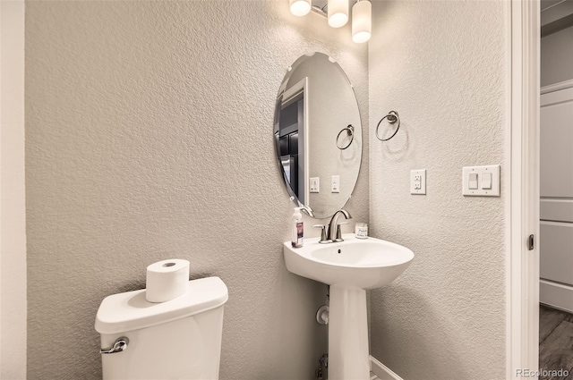 bathroom with toilet, a textured wall, and a sink