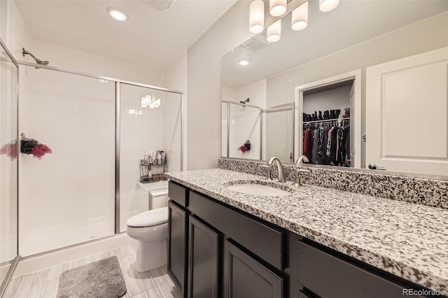 full bathroom with a walk in closet, a shower stall, toilet, and vanity