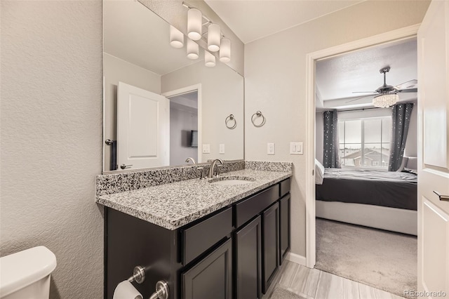 ensuite bathroom with toilet, vanity, a textured wall, ensuite bath, and a ceiling fan