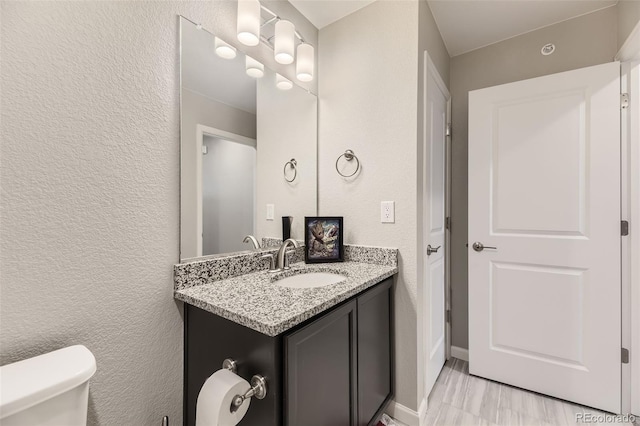 half bathroom featuring baseboards, toilet, vanity, and a textured wall