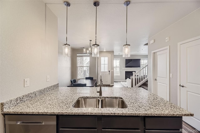 kitchen with a sink, light stone countertops, open floor plan, hanging light fixtures, and stainless steel dishwasher