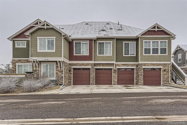 townhome / multi-family property featuring board and batten siding, an attached garage, stone siding, and driveway