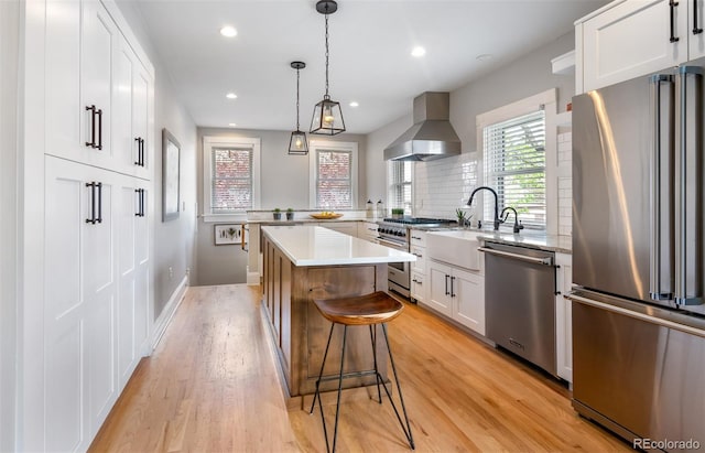 401 S Williams St, Denver, CO 80209 - kitchen featuring high end appliances, wall chimney exhaust hood, a sink, a center island, and light wood-style flooring