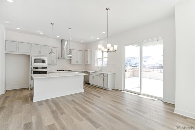 kitchen with pendant lighting, a kitchen island, light hardwood / wood-style flooring, wall chimney range hood, and stainless steel appliances