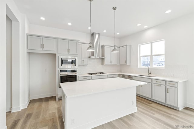 kitchen with a center island, sink, pendant lighting, wall chimney range hood, and appliances with stainless steel finishes