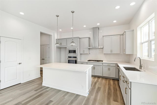 kitchen featuring wall chimney range hood, pendant lighting, sink, stainless steel appliances, and a center island