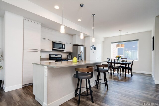 5630 W 11th Pl, Lakewood, CO 80214 - kitchen featuring appliances with stainless steel finishes, white cabinetry, an island with sink, baseboards, and dark wood finished floors