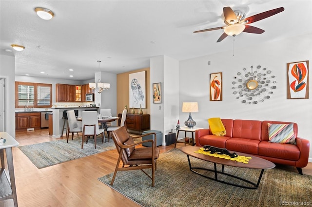 living room featuring sink, ceiling fan with notable chandelier, and light hardwood / wood-style flooring