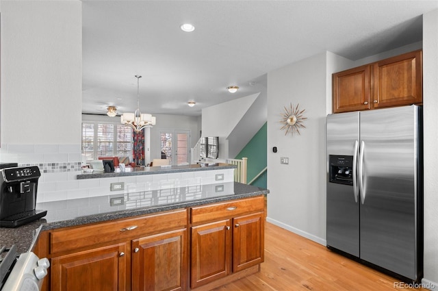 kitchen with light wood-type flooring, stainless steel fridge, hanging light fixtures, range, and tasteful backsplash