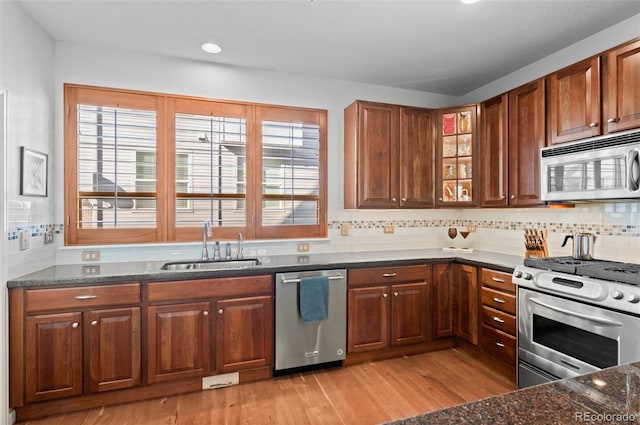 kitchen with dark stone countertops, sink, backsplash, light wood-type flooring, and stainless steel appliances