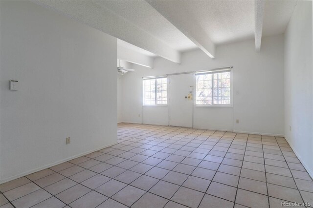 unfurnished room featuring beam ceiling, ceiling fan, light tile patterned floors, and a textured ceiling