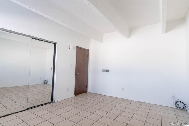 unfurnished bedroom with beamed ceiling, light tile patterned floors, and a closet