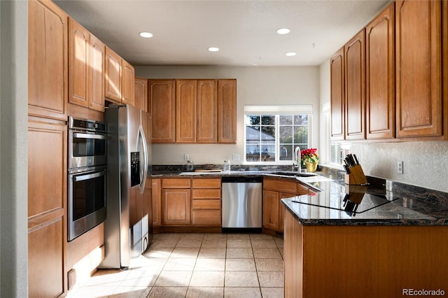 kitchen with kitchen peninsula, sink, appliances with stainless steel finishes, light tile patterned floors, and dark stone counters